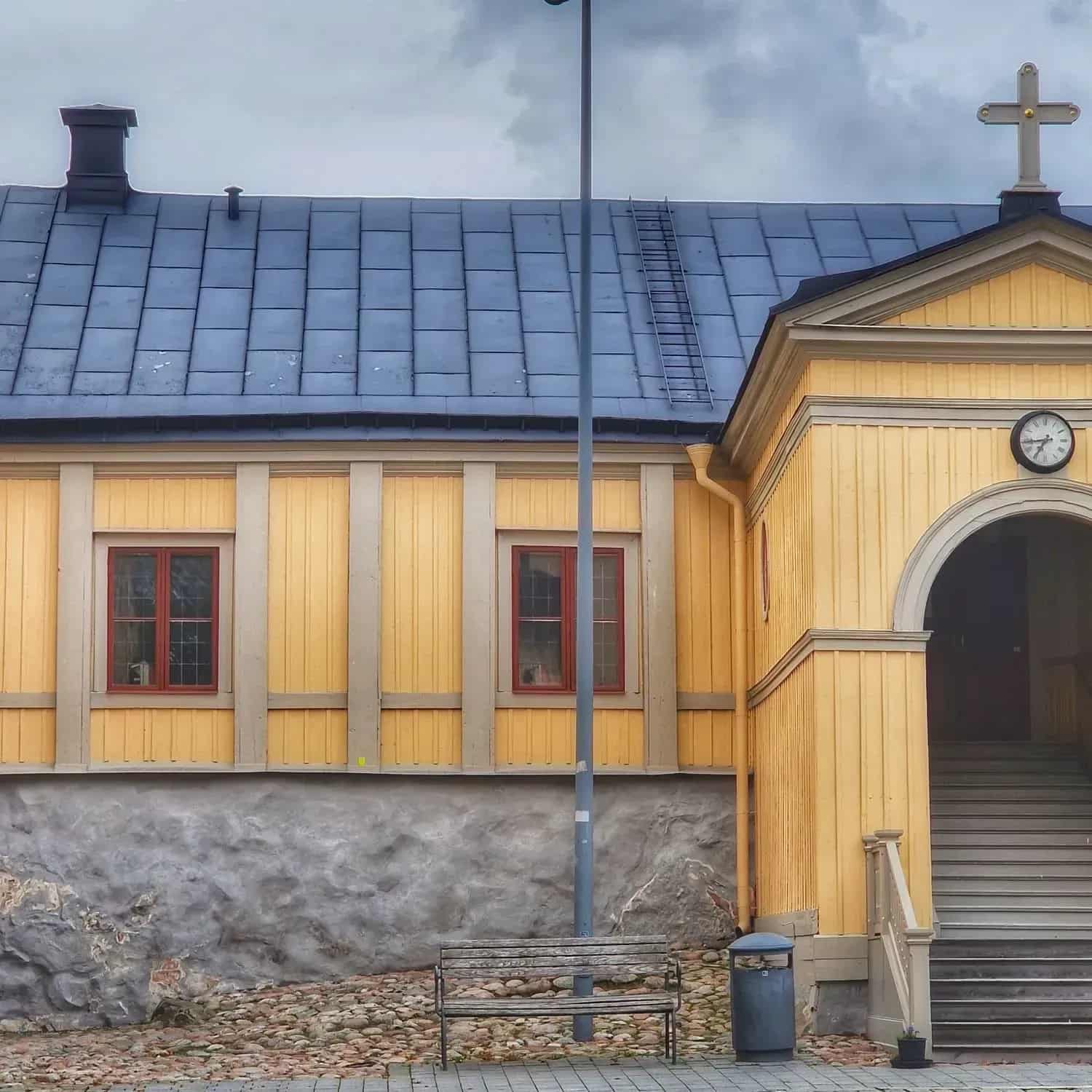 Gul byggnad med blått tegeltak, kors, stege, bänk och trappa