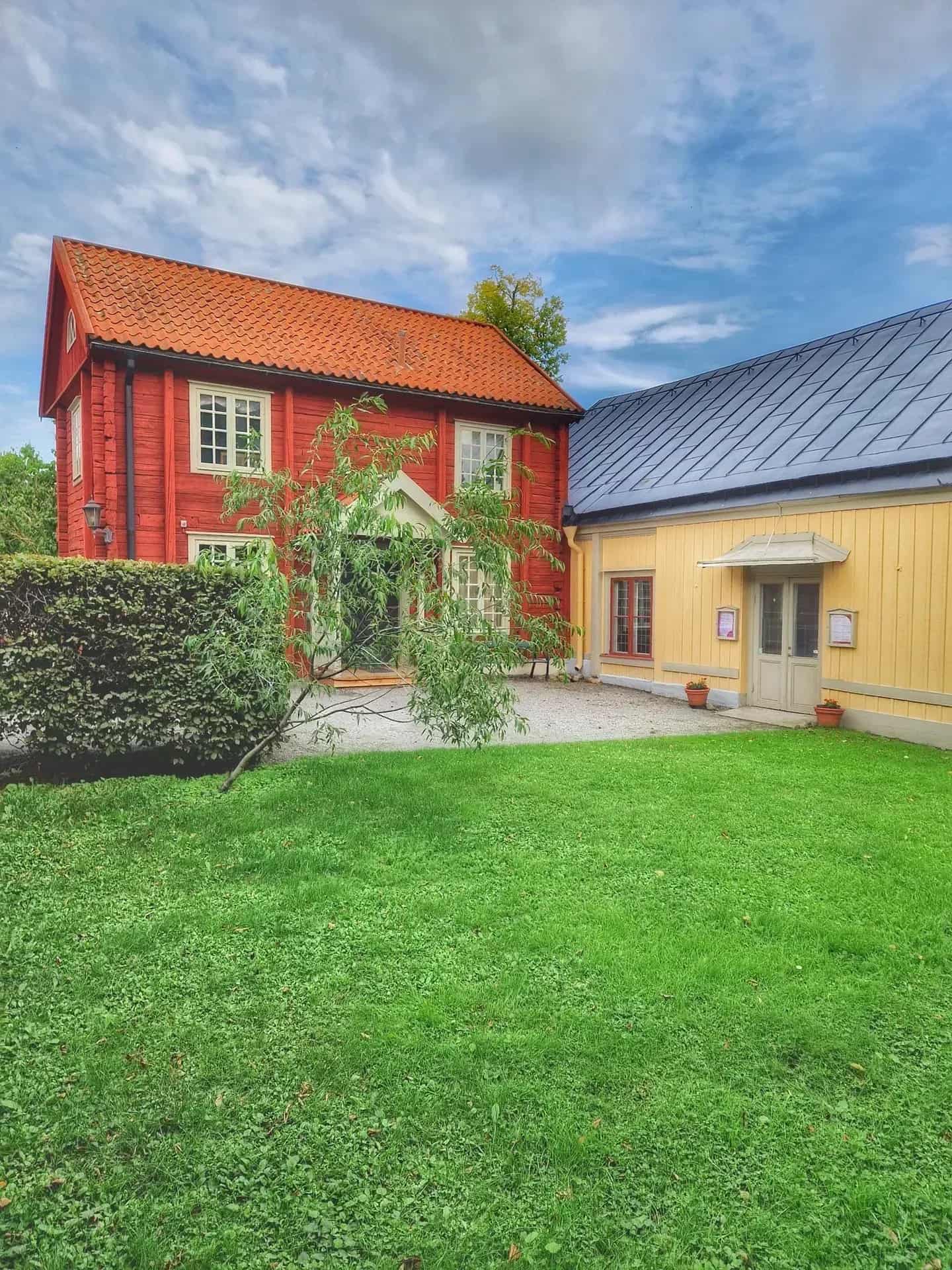 Red wooden house with tile roof, yellow wooden house with tin roof, lawn and blue sky