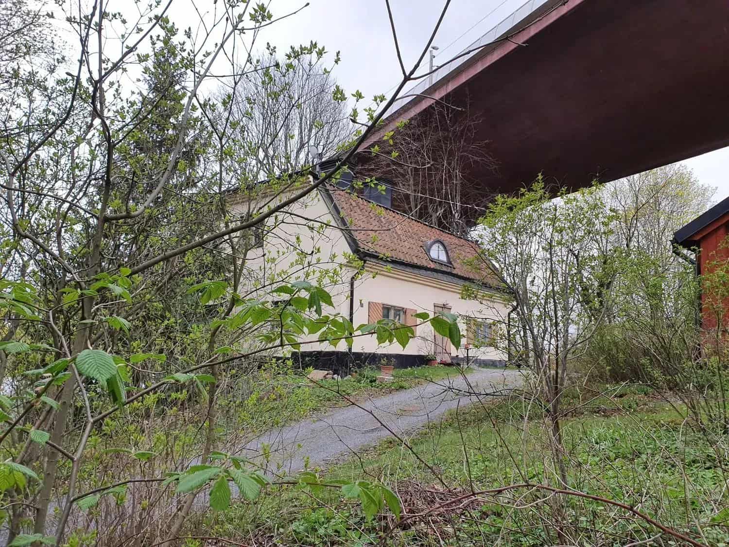 Hus med rött tak under bro. Buskar i förgrunden