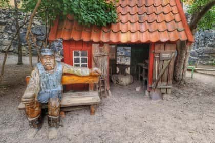 Träskulptur framför rött minihus med tegelpannor. Sandmark