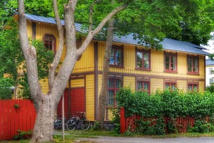 Gult trähus med röda detaljer, rött staket, två cyklar och träd