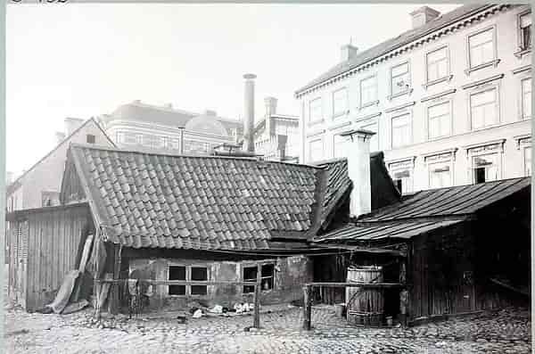 Older building with tiled roof, visible courtyard with cobblestones. Houses in the background