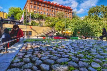 Stenbelagd plats med folk, bänkar och byggnad i bakgrunden. Aktiviteter stockholm kan hittas här