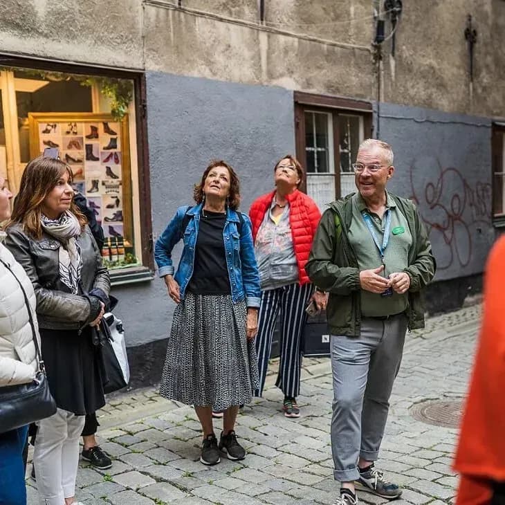 Group of people on a cobblestone street, some looking up. Shop window with shoes in the background