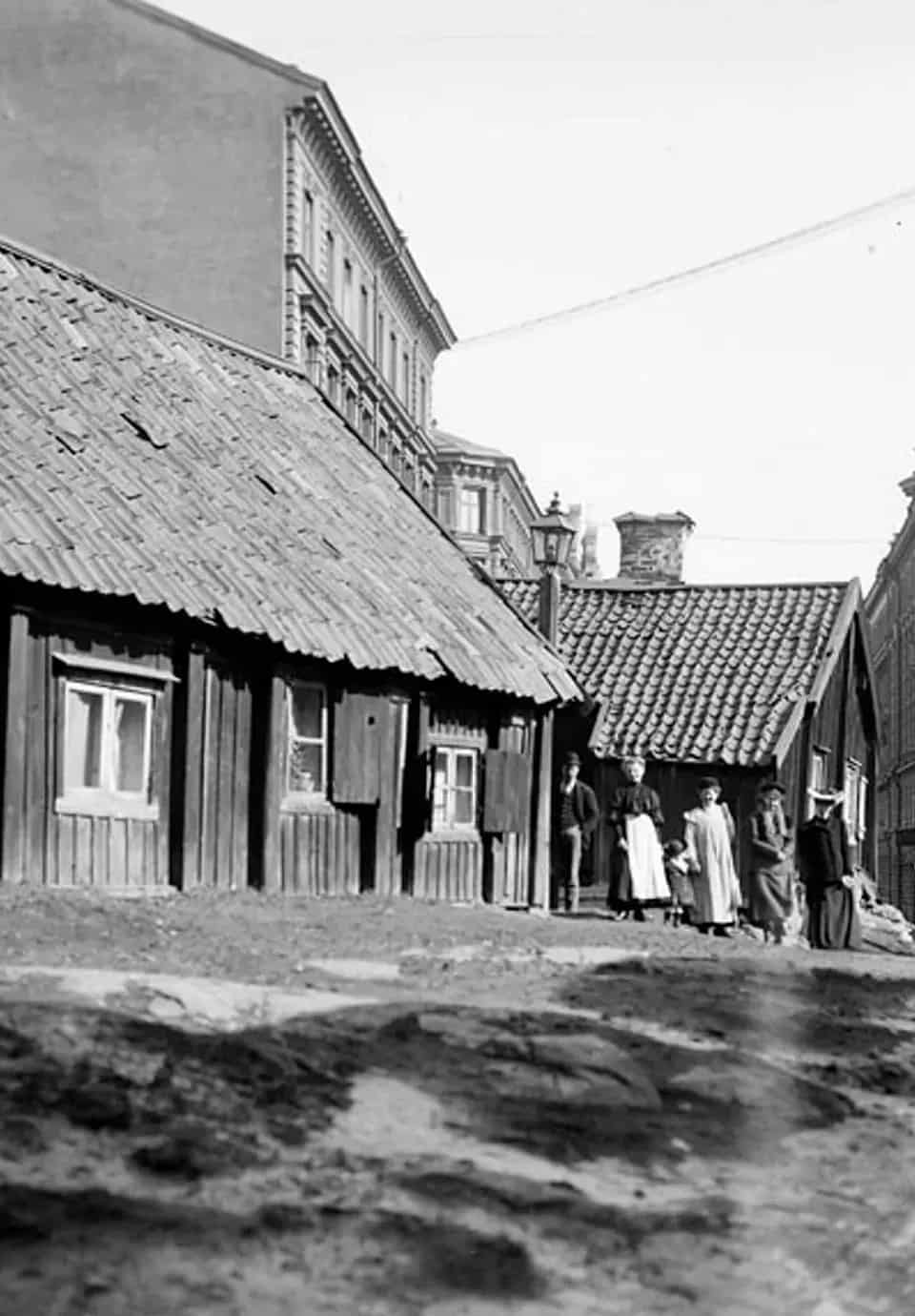 Svartvit bild av trähus, tegelhus och grupp människor