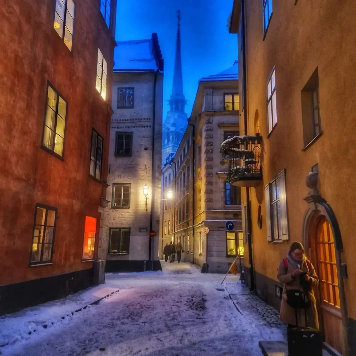 Gata i Gamla stan, Stockholm, med snö och en person med resväska. Kyrktorn syns